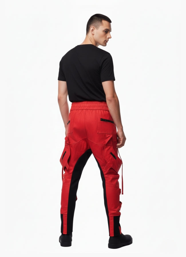 Rear view of man wearing red and black cyberpunk cargo pants with zipper pockets and tapered fit, styled with black t-shirt.