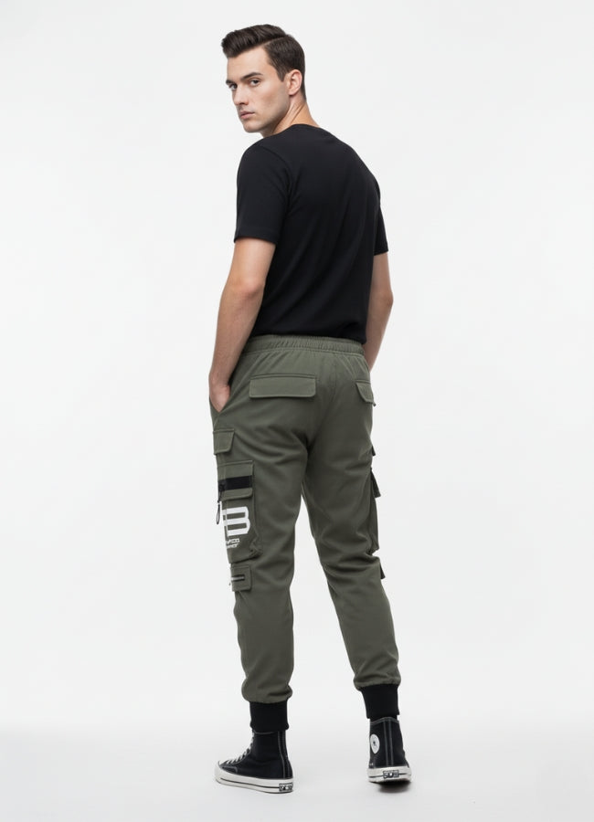 Back view of a man wearing khaki techwear cargo pants with multiple pockets and black detailing, paired with a black T-shirt and black high-top sneakers.