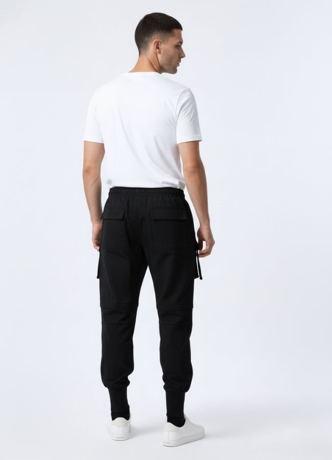 Bcak view of a man wearing black techwear sweatpants with large back pockets, paired with a white T-shirt and white sneakers.