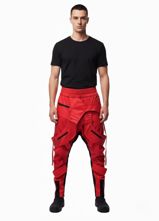 Male model wearing red techwear cargo pants with layered pocket design and elastic waist, paired with black t-shirt and shoes on white background.