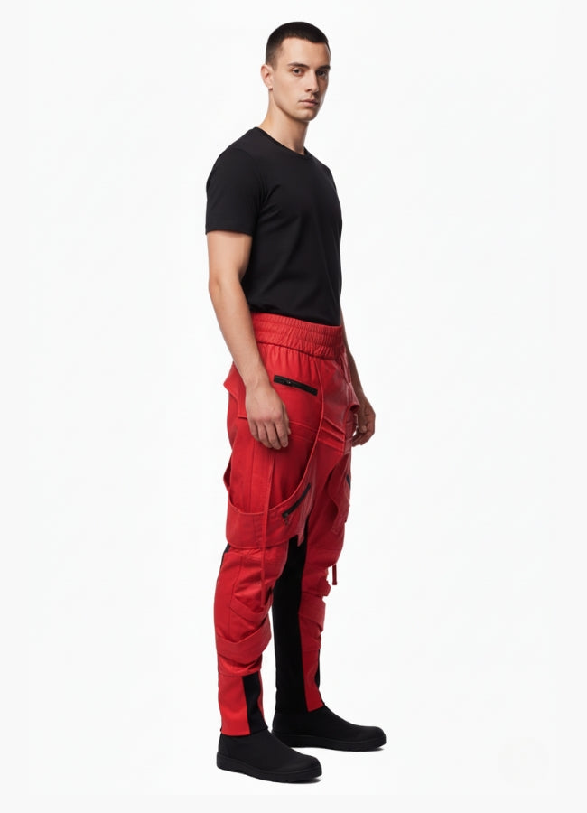 Side profile of male model dressed in red tactical techwear pants featuring straps and black side panels, styled with black t-shirt and shoes.