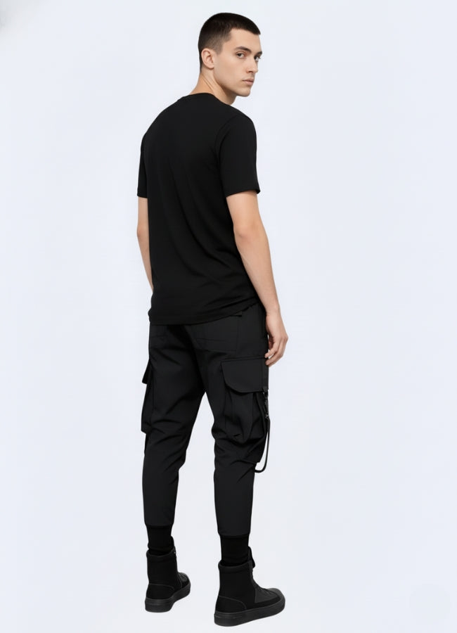 Rear view of black techwear cargo pants highlighting tapered fit, pocket placement, and adjustable ankle cuffs.