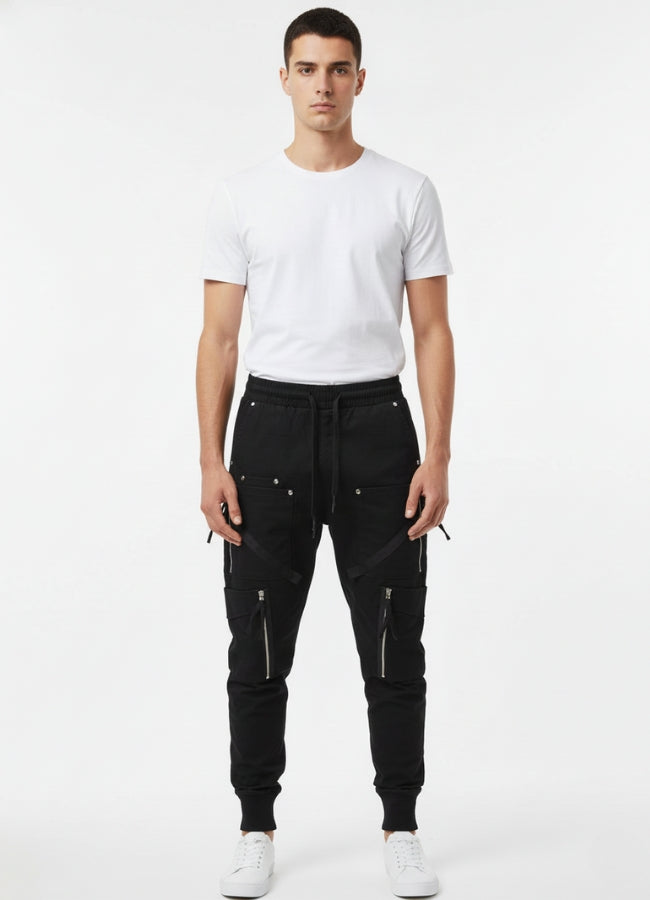 Man wearing black techwear skinny pants with multiple zipper pockets, standing front-facing in a white T-shirt and white sneakers