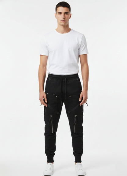 Man wearing black techwear skinny pants with multiple zipper pockets, standing front-facing in a white T-shirt and white sneakers