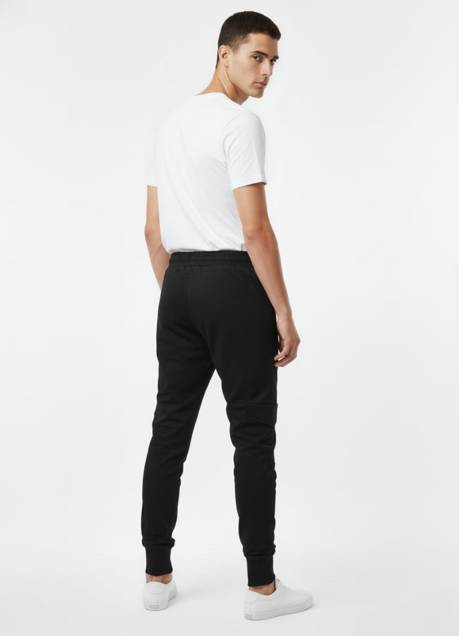 Back view of a man wearing black techwear skinny pants with cuffed ankles, shown with a white T-shirt and white sneakers