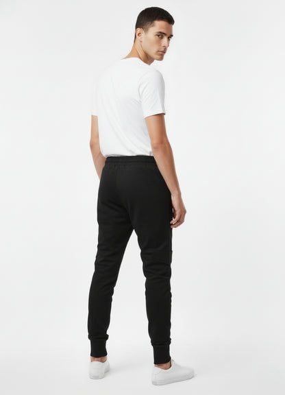 Back view of a man wearing black techwear skinny pants with cuffed ankles, shown with a white T-shirt and white sneakers