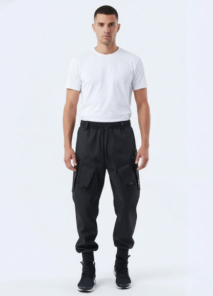 Male model wearing futuristic techwear cargo pants with utility pockets and tapered cuffs, styled with white t-shirt and sneakers.