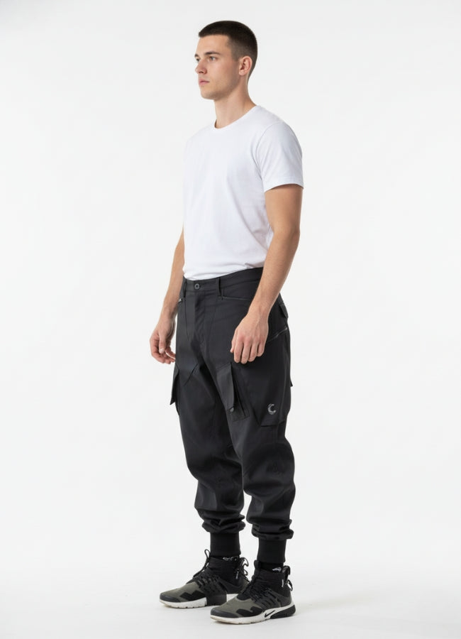 Side angle of black futuristic cargo pants showcasing pocket structure, articulated knees, and modern urban fit.