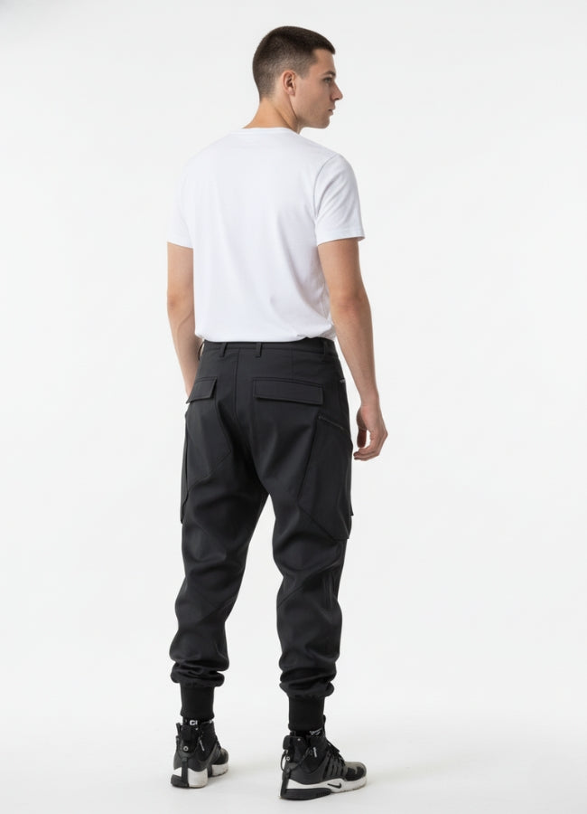 Rear view of black techwear pants featuring dual back pockets and ribbed ankle cuffs, paired with minimalist white tee.