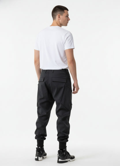 Rear view of black techwear pants featuring dual back pockets and ribbed ankle cuffs, paired with minimalist white tee.