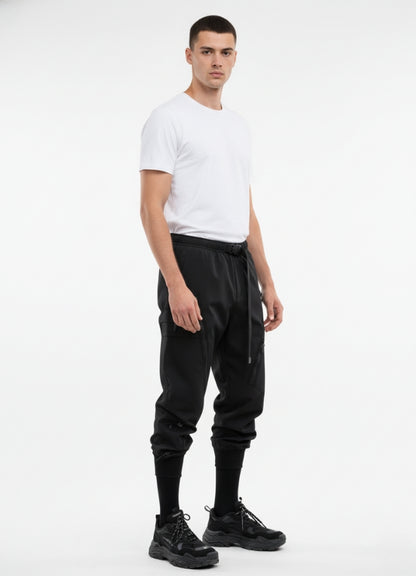 Side angle of black techwear pants featuring adjustable belt, multi-pocket design, and tapered ankle cuffs.