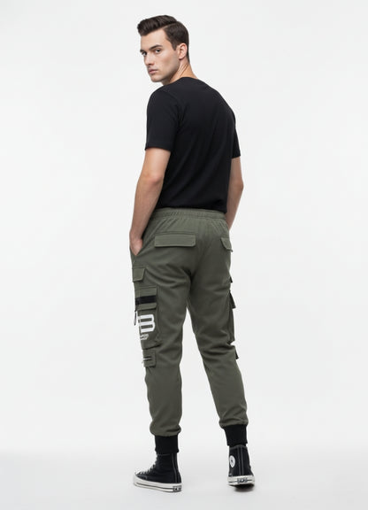 Back view of a man wearing khaki techwear cargo pants with multiple pockets and black detailing, paired with a black T-shirt and black high-top sneakers.