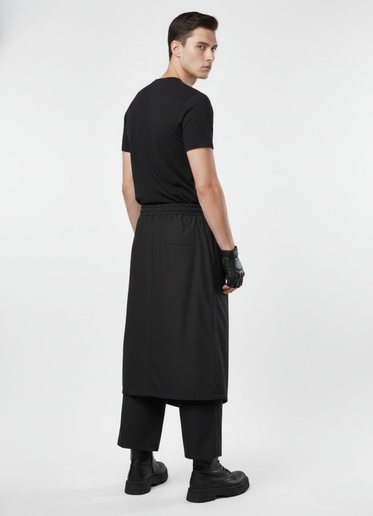 Rear view of black techwear skirt trousers featuring elastic waist and sleek layered silhouette, styled with black top and boots.