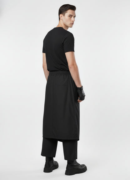 Rear view of black techwear skirt trousers featuring elastic waist and sleek layered silhouette, styled with black top and boots.