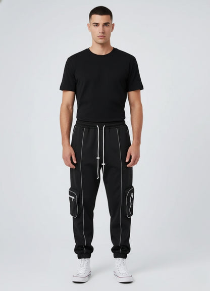 Male model wearing black techwear jogger pants with white reflective and utility side pockets, styled with black t-shirt and white sneakers.
