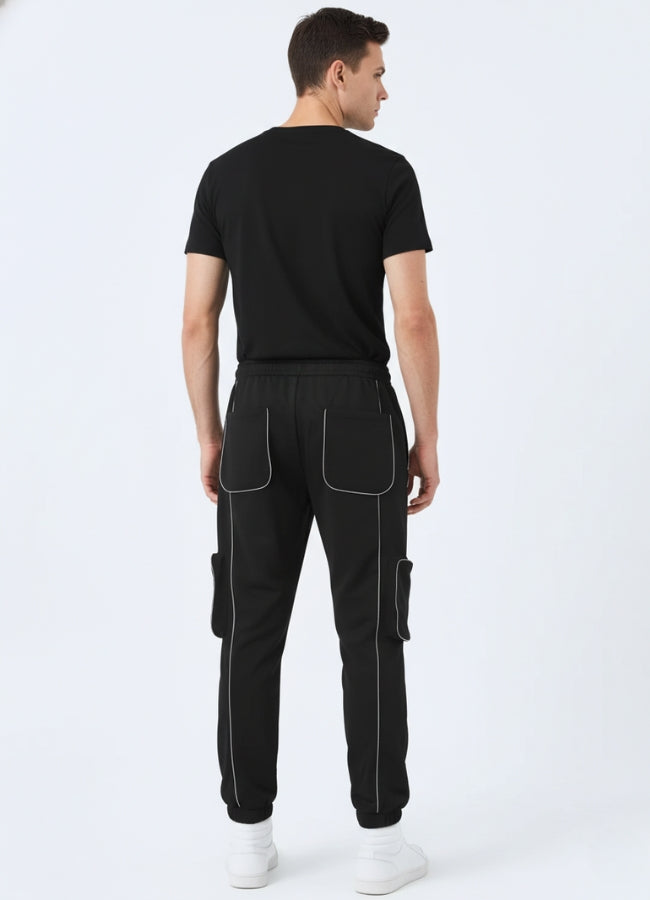 Rear view of black techwear pants highlighting reflective stitching, elastic waistband, and dual patch pockets.