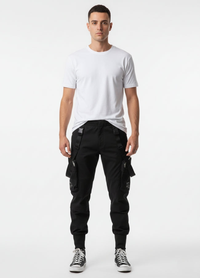 Male model wearing black techwear cropped pants with straps and zipper pockets, paired with plain white t-shirt and sneakers.