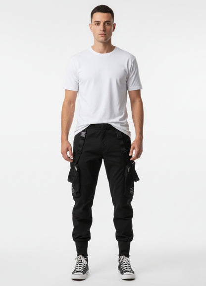 Male model wearing black techwear cropped pants with straps and zipper pockets, paired with plain white t-shirt and sneakers.