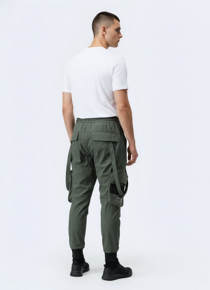 Rear view of green techwear cropped pants featuring pockets, strap details, and elastic cuffs, paired with minimalist white tee