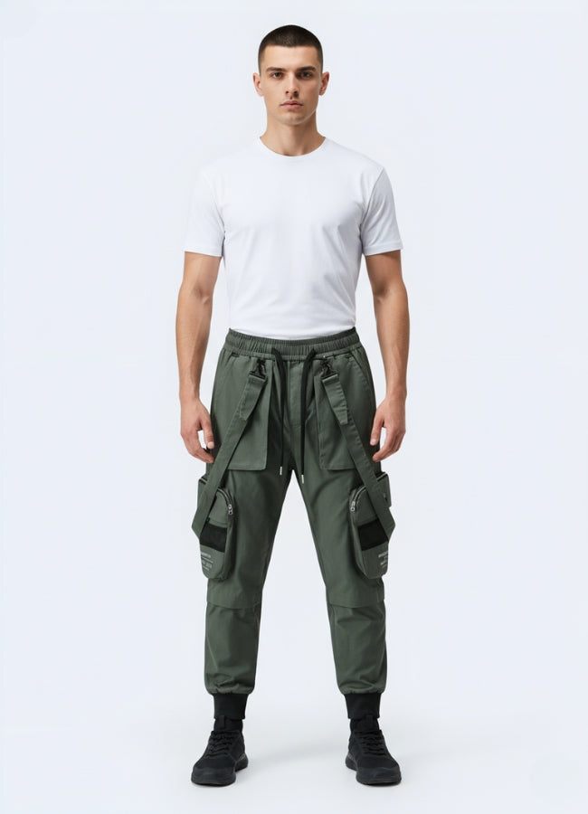 Male model wearing green techwear cropped pants with straps and oversized utility pockets, styled with white t-shirt and black sneakers.