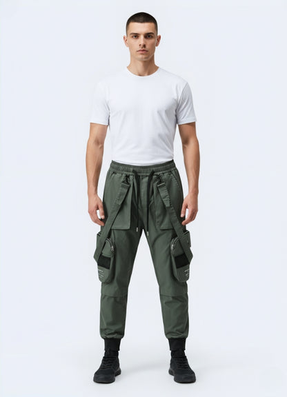 Male model wearing green techwear cropped pants with straps and oversized utility pockets, styled with white t-shirt and black sneakers.