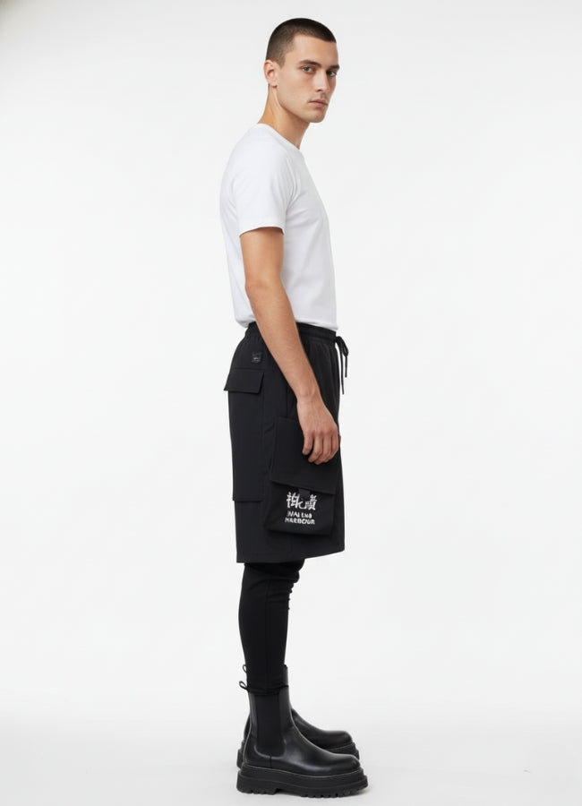 Side angle of techwear leggings short with layered pocket design and white text graphic, styled with white t-shirt and black boots.