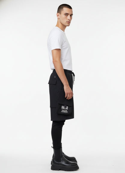 Side angle of techwear leggings short with layered pocket design and white text graphic, styled with white t-shirt and black boots.