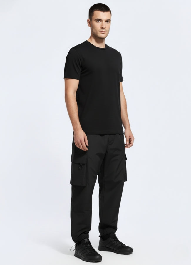 Side angle of black tactical cargo pants featuring structured silhouette and utility pockets, paired with fitted black t-shirt and sneakers.