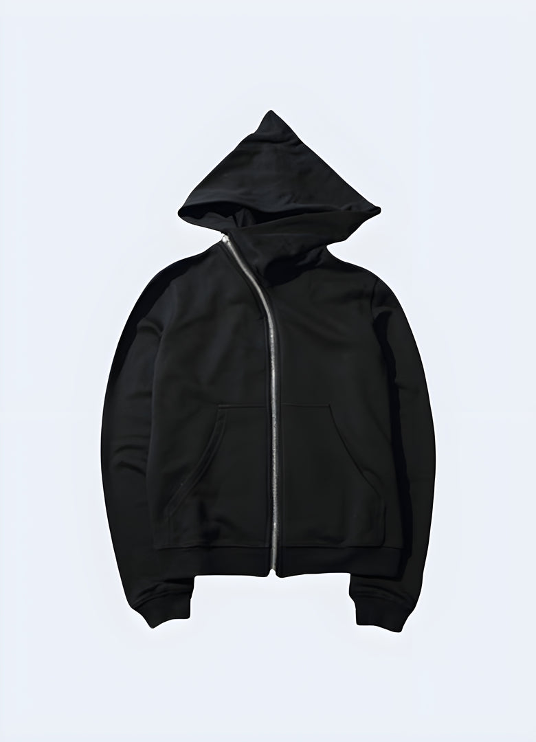 Front view of a person in a black zip-up hoodie featuring a skull and crossed swords graphic, with their hands in the pockets, standing in a dimly lit city environment.