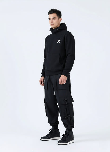 Person wearing a black hoodie and cargo pants with a white logo on a white background