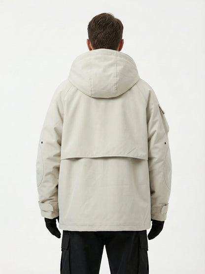 Rear view of the male model showing the back of the beige techwear jacket, featuring a large hood, a back yoke flap design, a sleeve pocket, and adjustable cuffs, paired with black cargo pants and gloves.