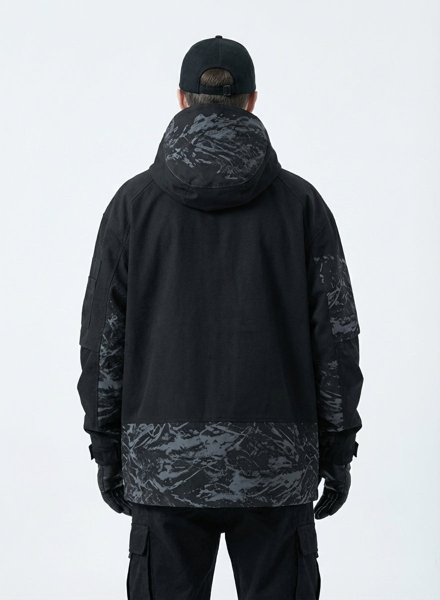Rear view of male model in a black techwear jacket showing the grey abstract camouflage pattern on the hood, back panel, and sleeves, with black cargo pants and a black baseball cap.