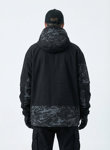 Rear view of male model in a black techwear jacket showing the grey abstract camouflage pattern on the hood, back panel, and sleeves, with black cargo pants and a black baseball cap.